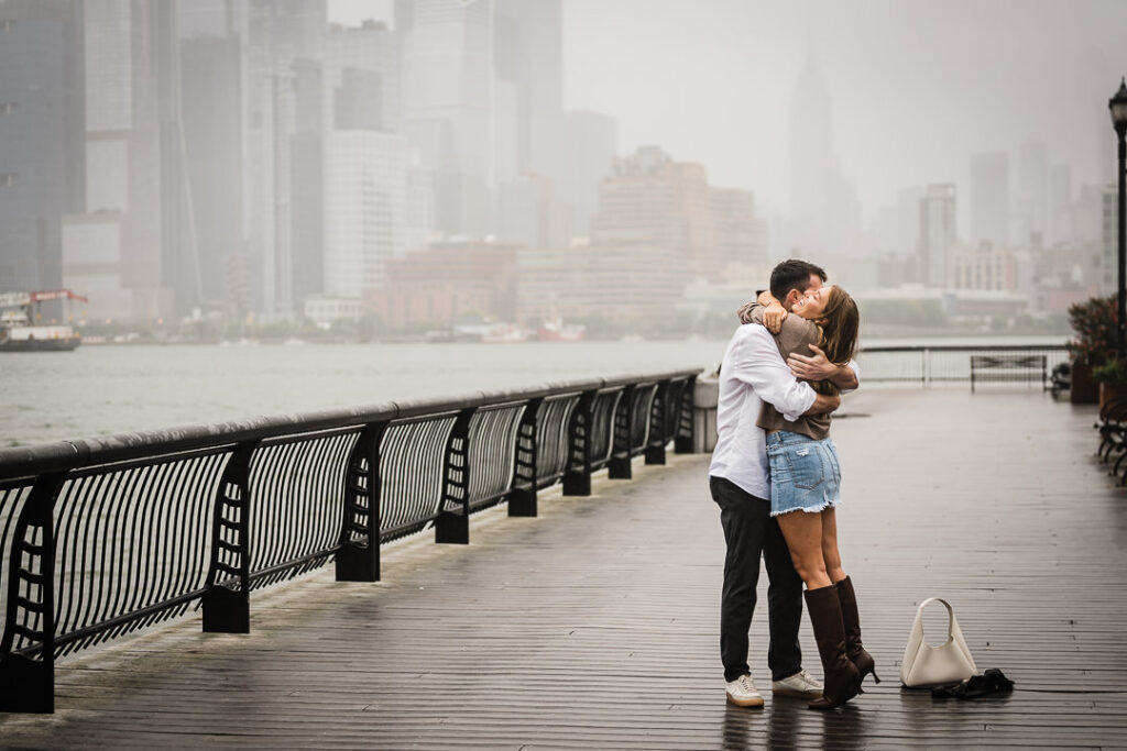 Couple kissing on rainy Pier 13 boardwalk after getting engaged with foggy cityscape behind