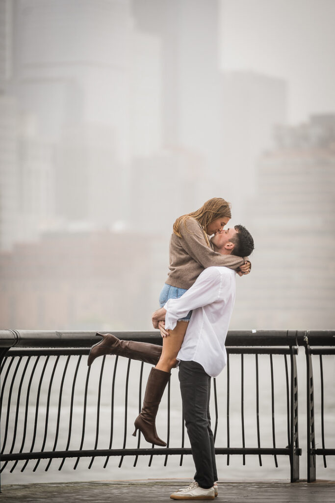 Groom lifting excited bride in celebration after engagement on Pier 13 with foggy cityscape background