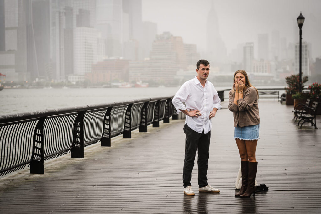 Excited newly engaged woman covering her face in surprise during Pier 13 proposal in Hoboken
