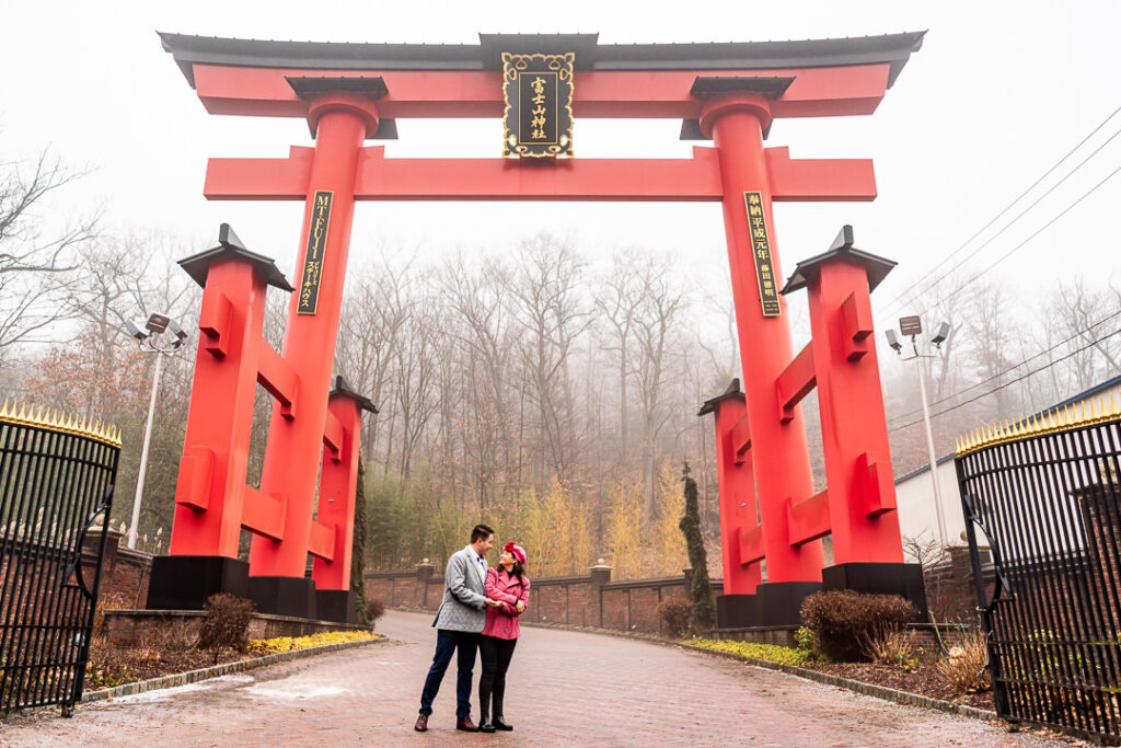 Wide angle of engaged couple standing under massive torii gate at Mount Fuji venue.