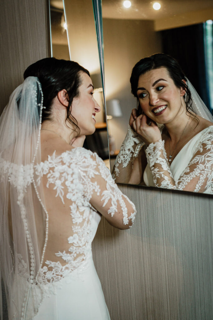 Bride laughing while getting ready at mirror by Alex Kaplan