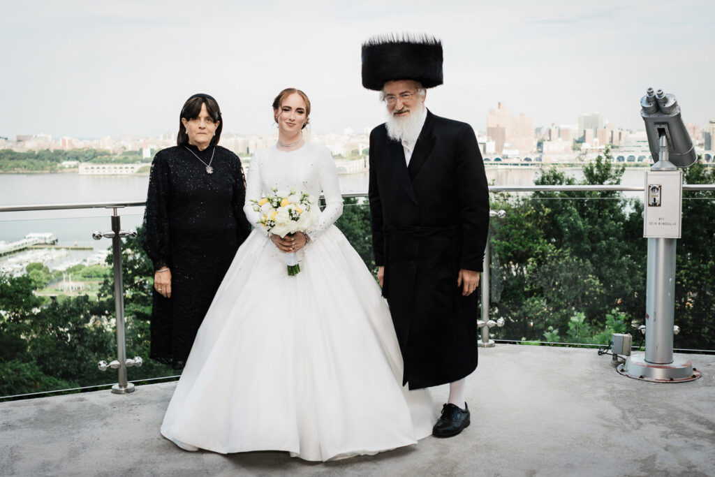 Bride with parents overlooking Hudson River and NYC skyline at Riverview Ballroom Cliffside Park Orthodox wedding