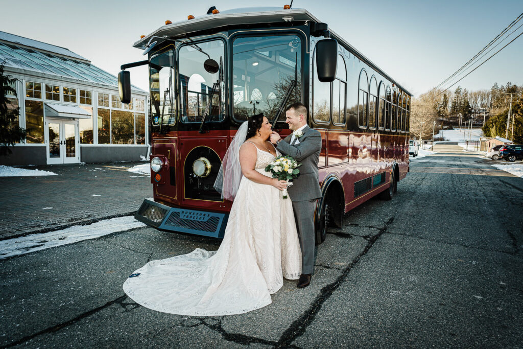 Couple embracing in front of vintage burgundy trolley at Sussex County Fairgrounds winter wedding by Alex Kaplan