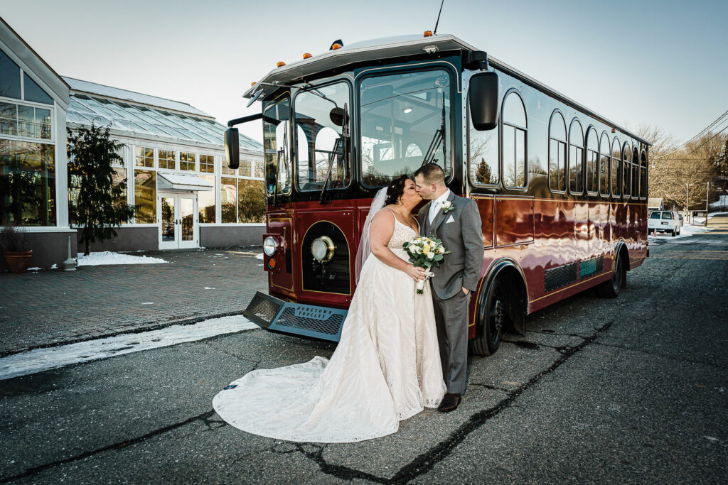 Bride and groom kissing in front of vintage trolley at The Conservatory Sussex County Fairgrounds by Alex Kaplan Photography
