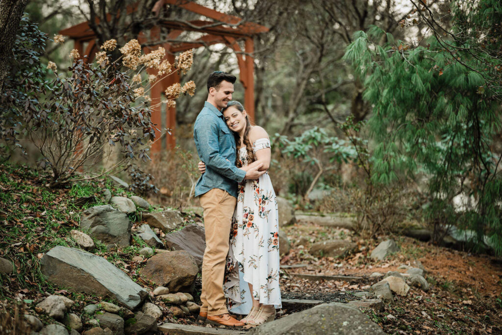 Engaged couple embraces by rock garden and wooden pergola at Sayen House and Gardens winter engagement photos