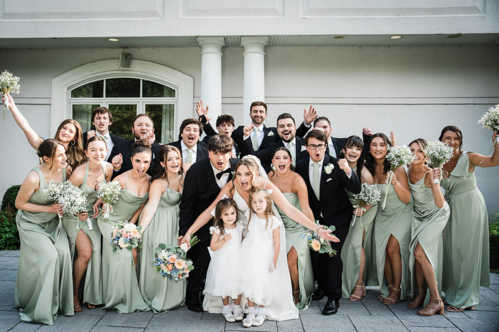 Complete wedding party with bridesmaids in sage green dresses celebrating outside Mansion at Mountain Lakes