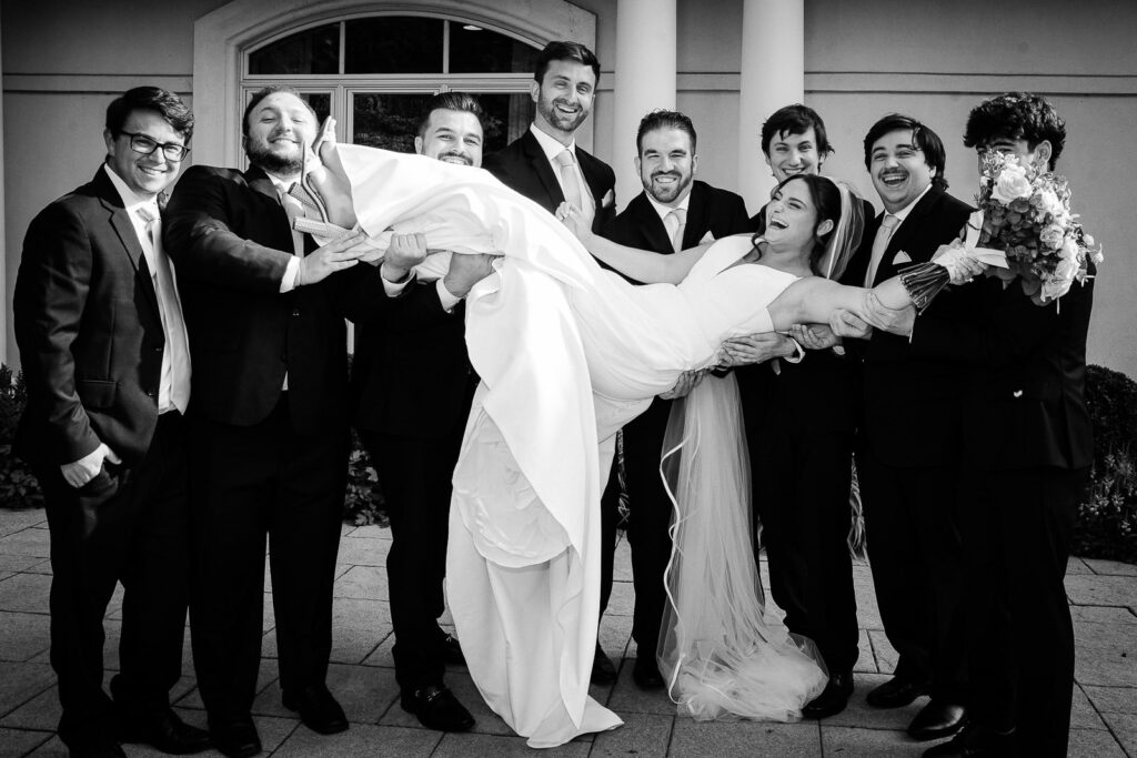 Groomsmen lifting bride in playful black and white photo at Mansion at Mountain Lakes