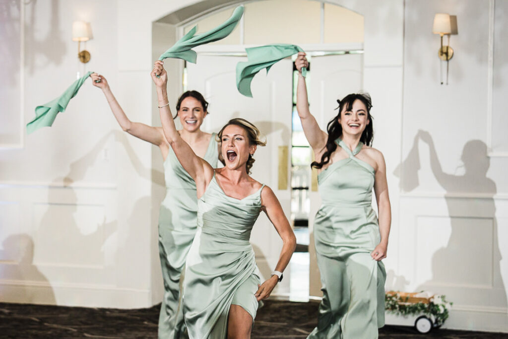 Bridesmaids in sage green dresses making energetic entrance at Mansion at Mountain Lakes ballroom