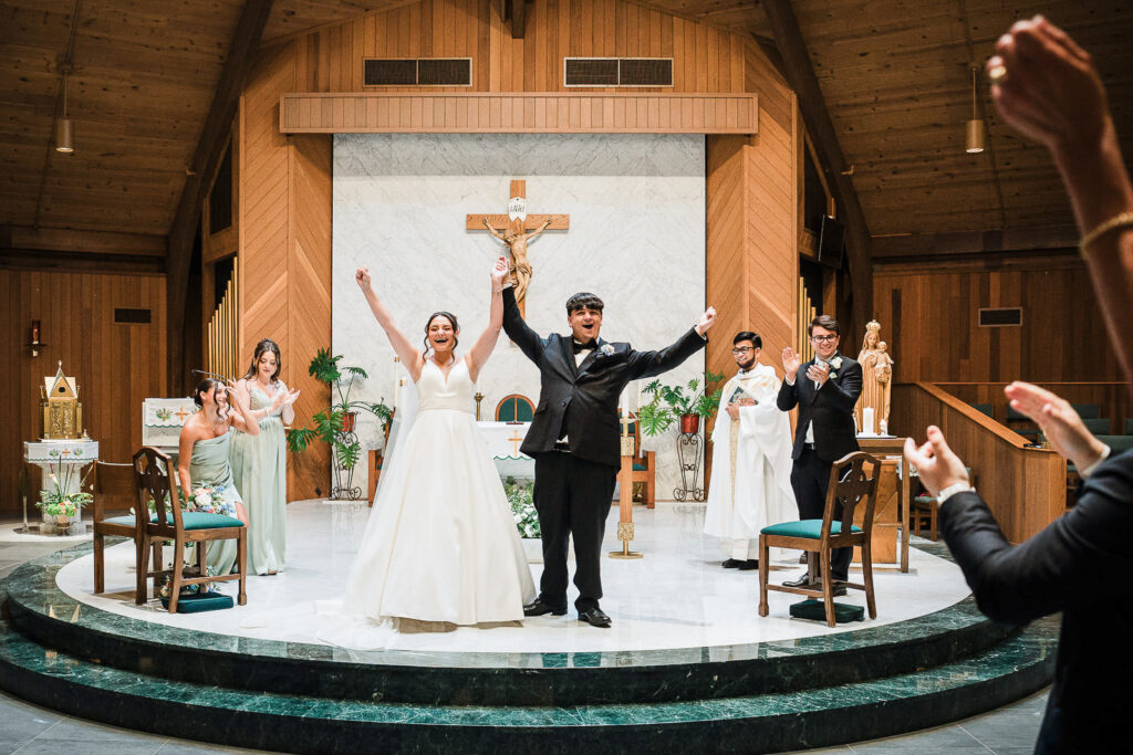 Newlyweds raising hands in celebration after Catholic ceremony at Notre Dame of Mt Carmel
