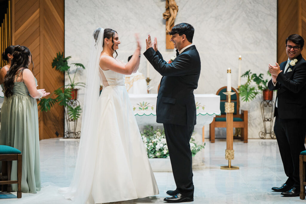 Newlyweds celebrating with high five during ceremony at Notre Dame of Mt Carmel Church