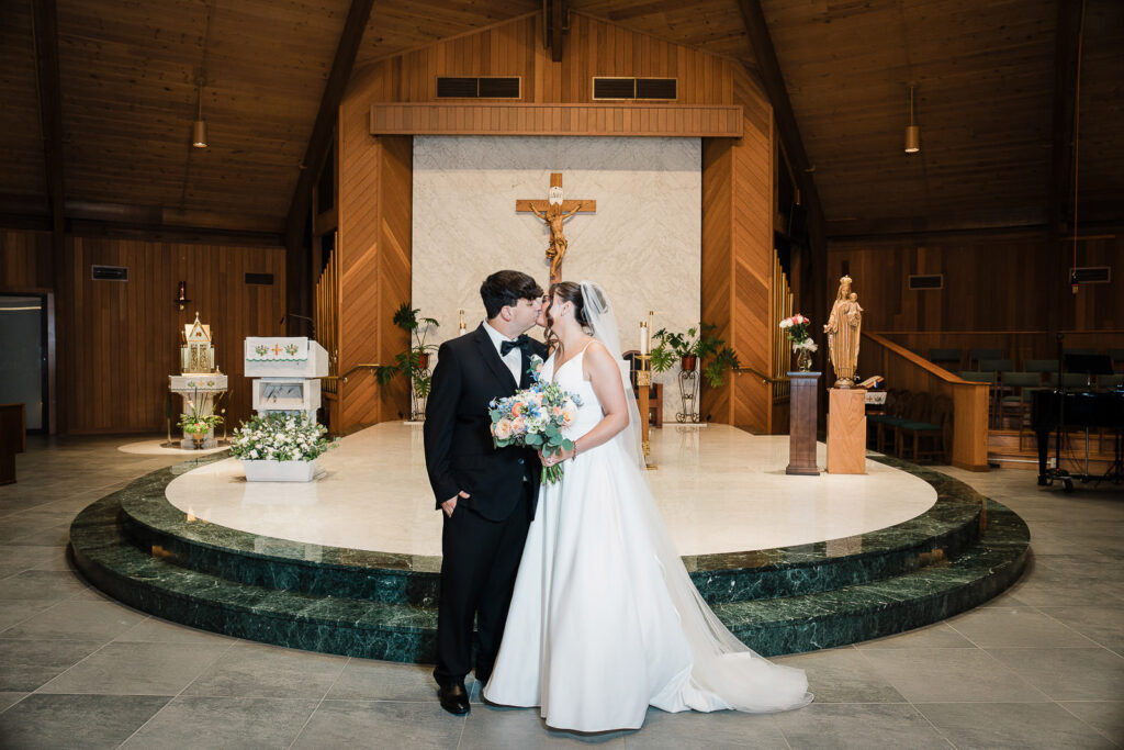 Newlyweds sharing kiss at Notre Dame of Mt Carmel Church altar after Catholic ceremony