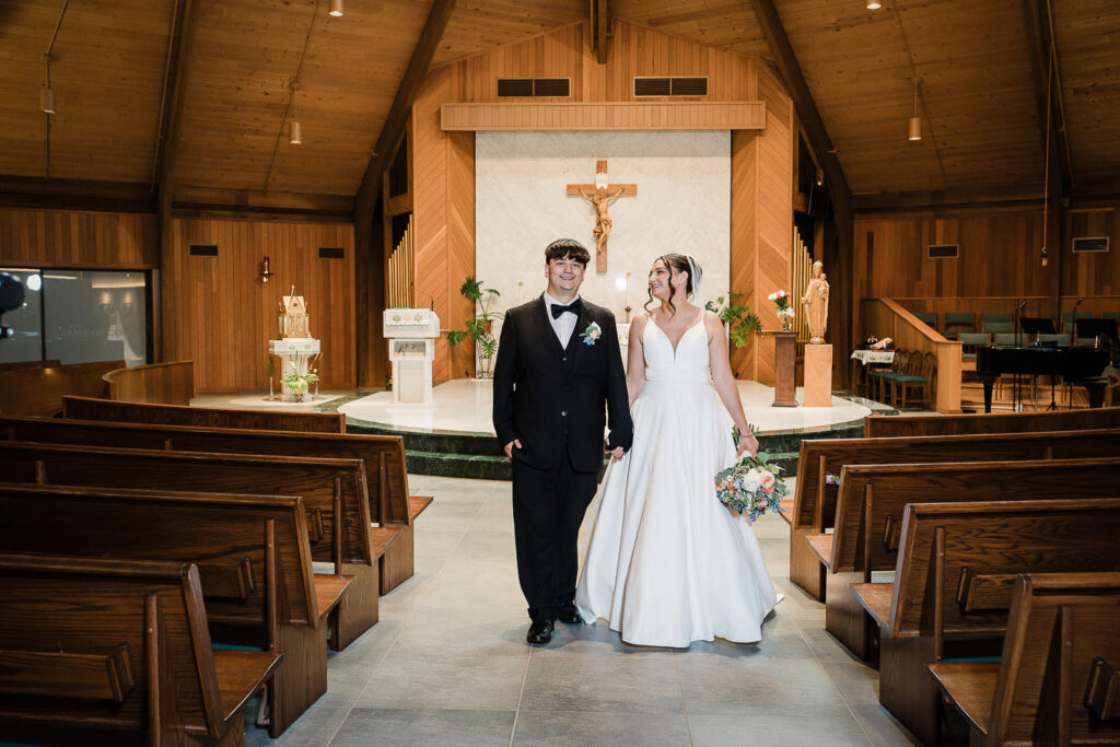 Bride and groom walking hand in hand down aisle at Notre Dame of Mt Carmel Church as married couple