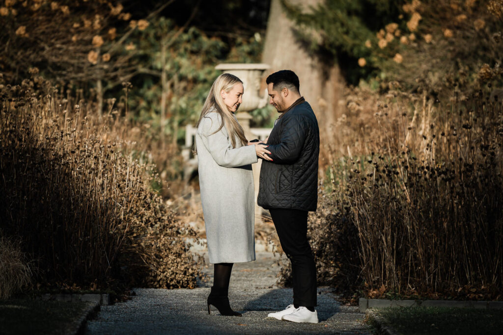 Newly engaged couple standing together at Van Vleck Gardens Montclair with ornamental grasses and white bench