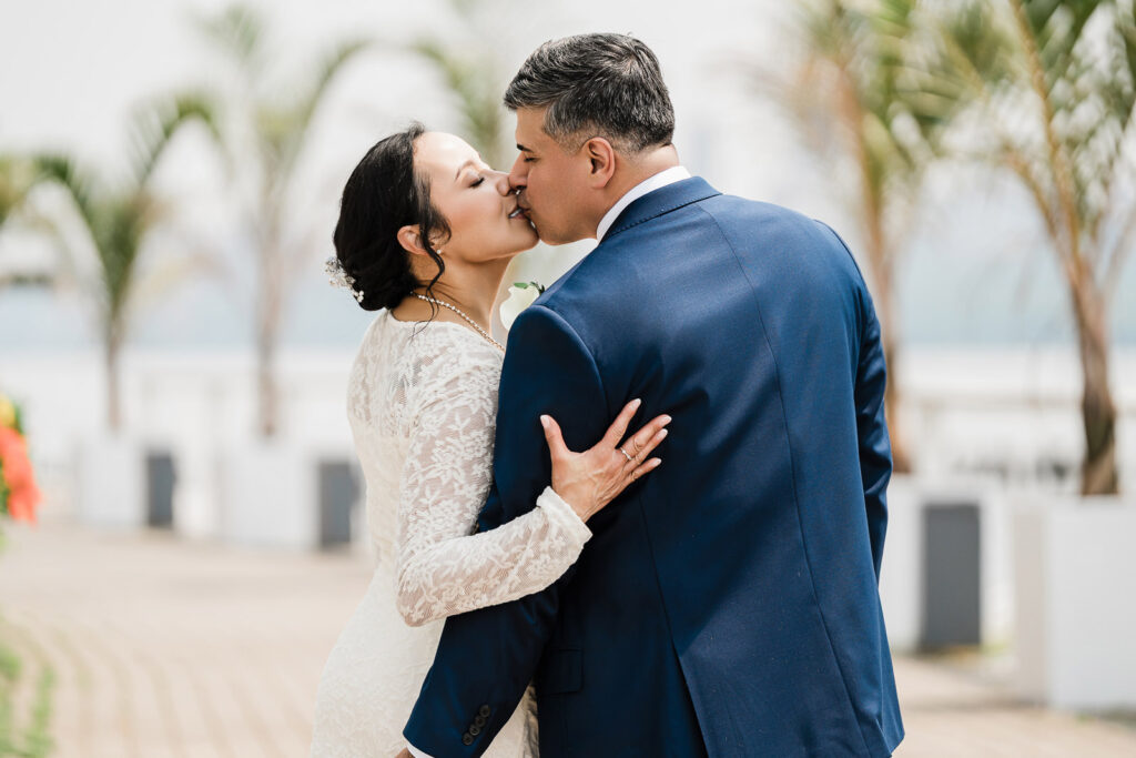 Wedding rings detail with couple kissing in background at Waterside by photographer Alex Kaplan