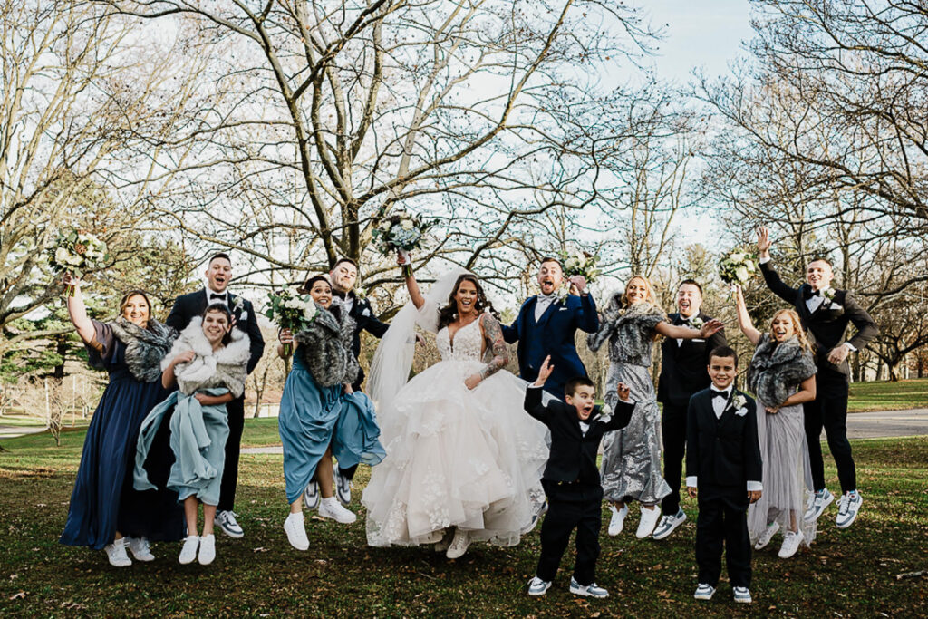 Wedding party jumping in celebration at Thompson Park with matching white sneakers before 618 Restaurant Freehold Township wedding by NJ photographer Alex Kaplan
