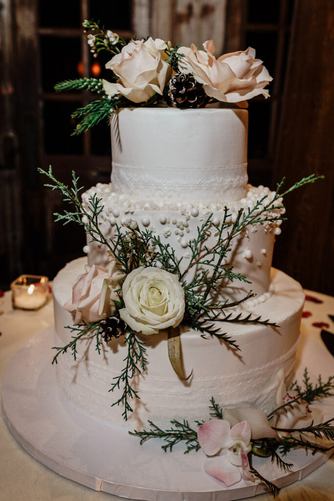 Three-tier white wedding cake with roses and greenery by Alex Kaplan Photography