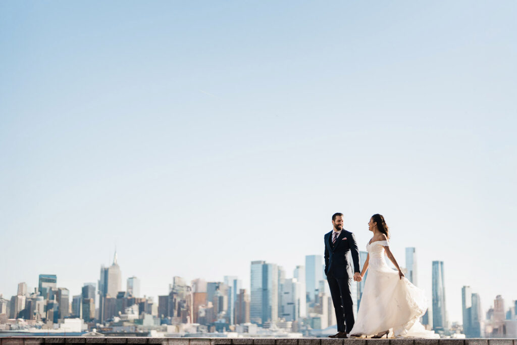 Joanna and Alex romantic moment on waterfront wall with full NYC skyline Port Imperial wedding photography