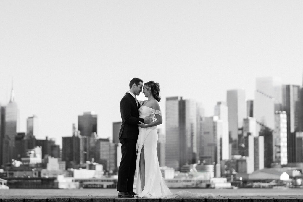 Black and white Luz and Stephan embracing with Manhattan skyline Port Imperial timeless wedding photography West New York