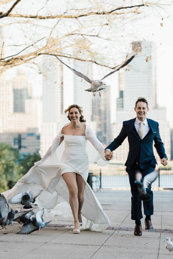 Luz and Stephan laughing with seagull flying and NYC skyline Port Imperial authentic wedding moment West New York photographer