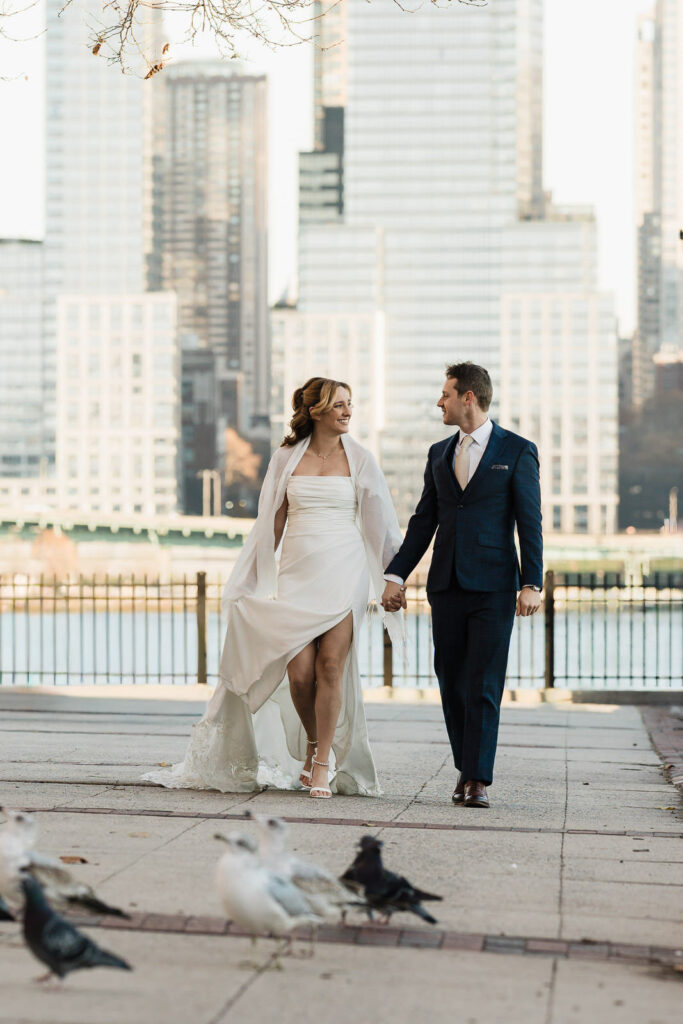 Luz and Stephan walking with pigeons on Port Imperial promenade NYC skyline candid wedding photography West New York