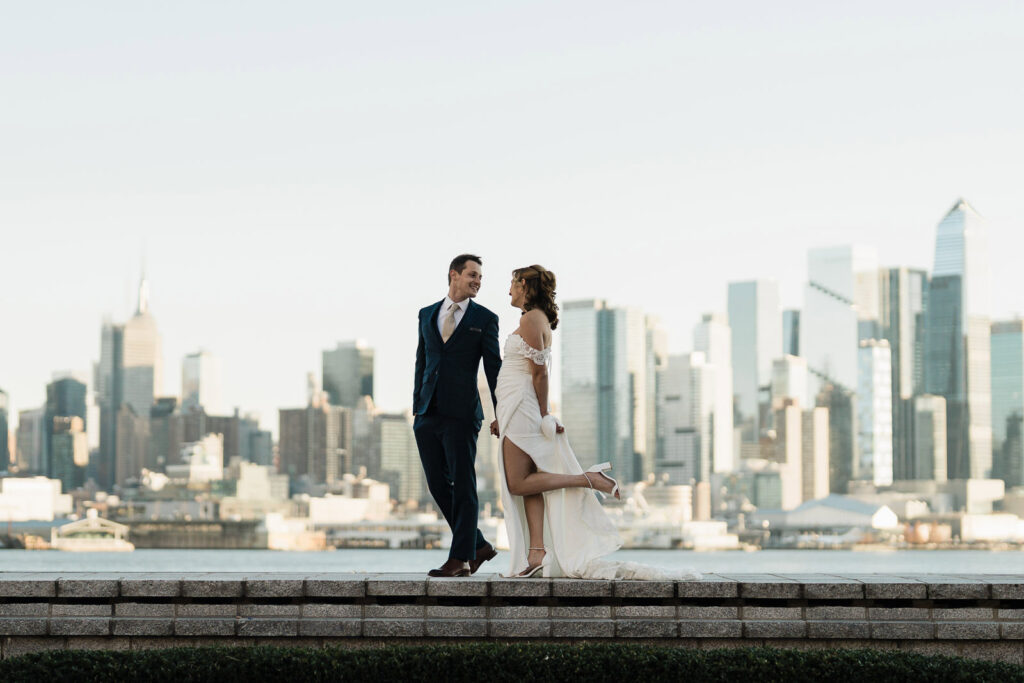 Luz and Stephan standing on waterfront wall with NYC skyline intimate wedding portrait Port Imperial West New York NJ