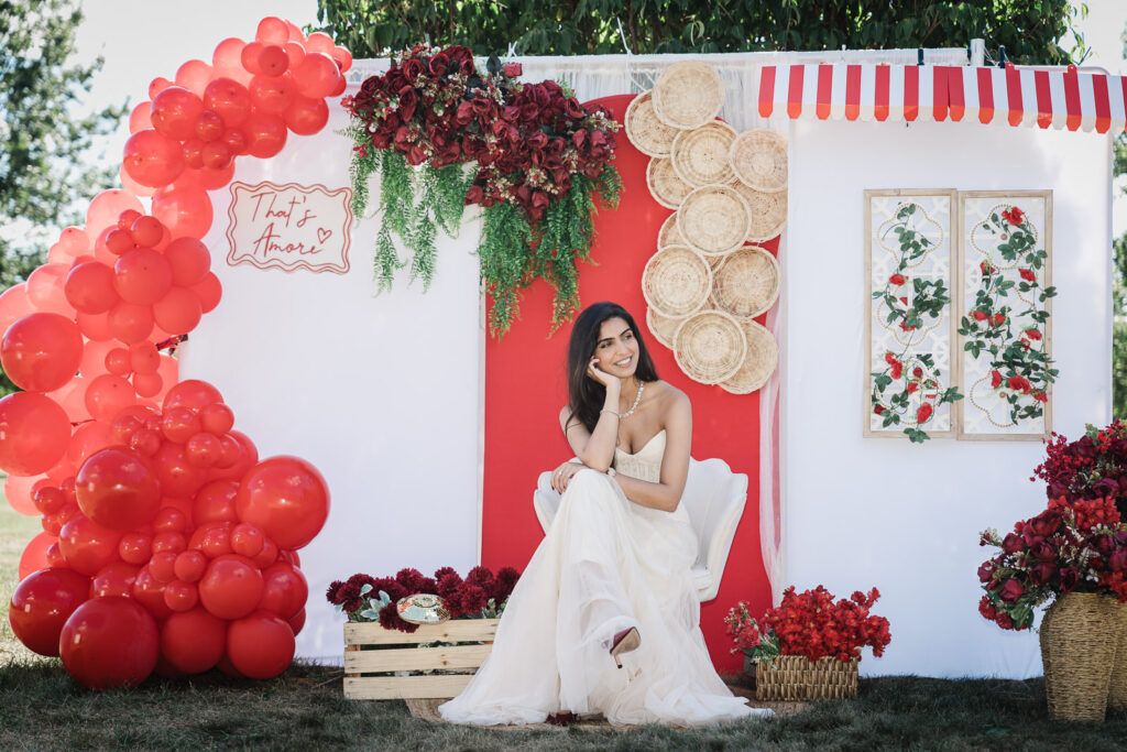 Bride in white gown with red balloon arch and woven plate backdrop