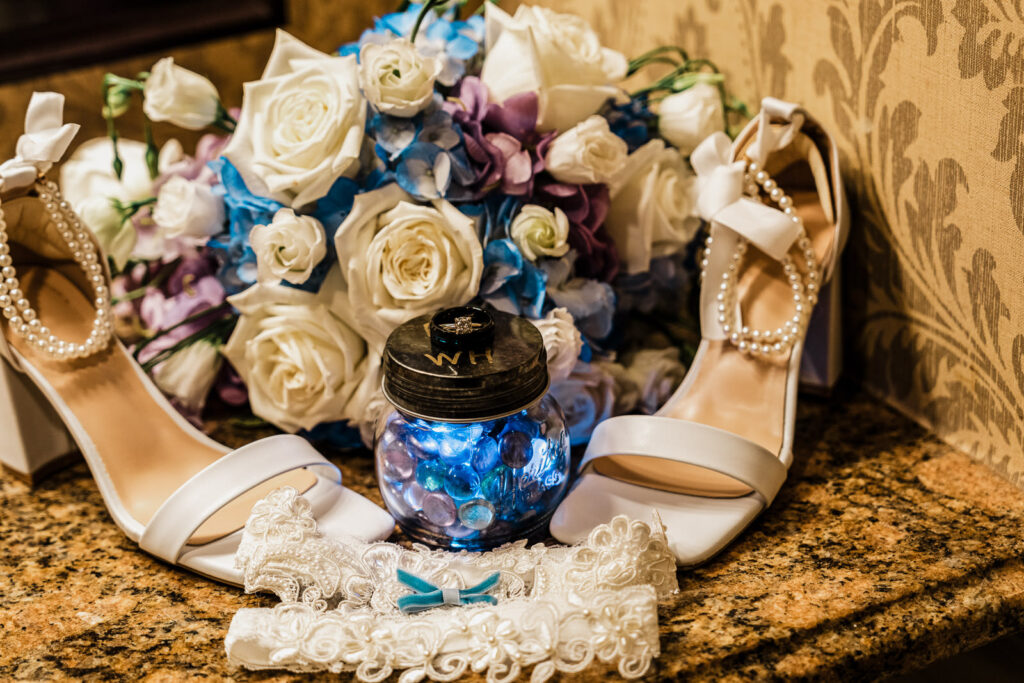 bridal-details-shoes-bouquet-garter-nj.jpgWedding day bridal details including white pearl shoes, blue and purple bouquet, lace garter and personalized ring jar at Smithville Inn