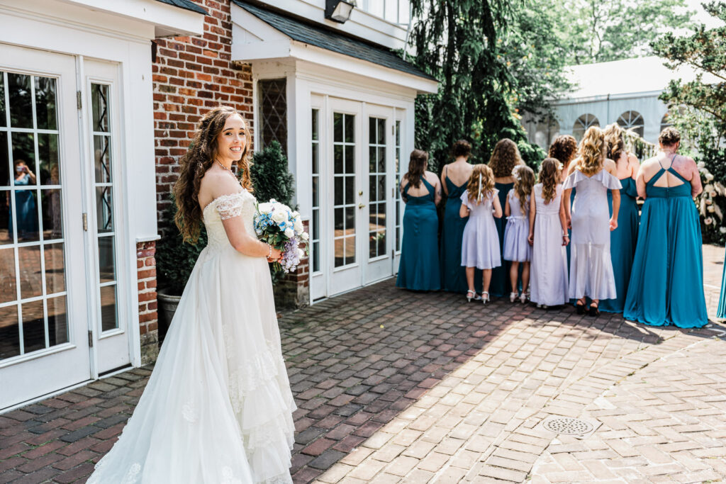 Bride in full wedding dress doing first look with bridesmaids in brick courtyard at Smithville Inn Absecon New Jersey