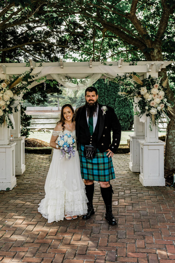 Bride and Scottish groom formal portrait standing under white floral pergola at Smithville Inn lakeside ceremony in Absecon New Jersey