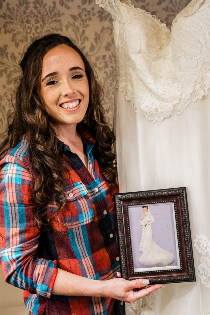 Bride in flannel shirt emotionally holding framed photo of mother in wedding dress with her own gown displayed at Smithville Inn NJ