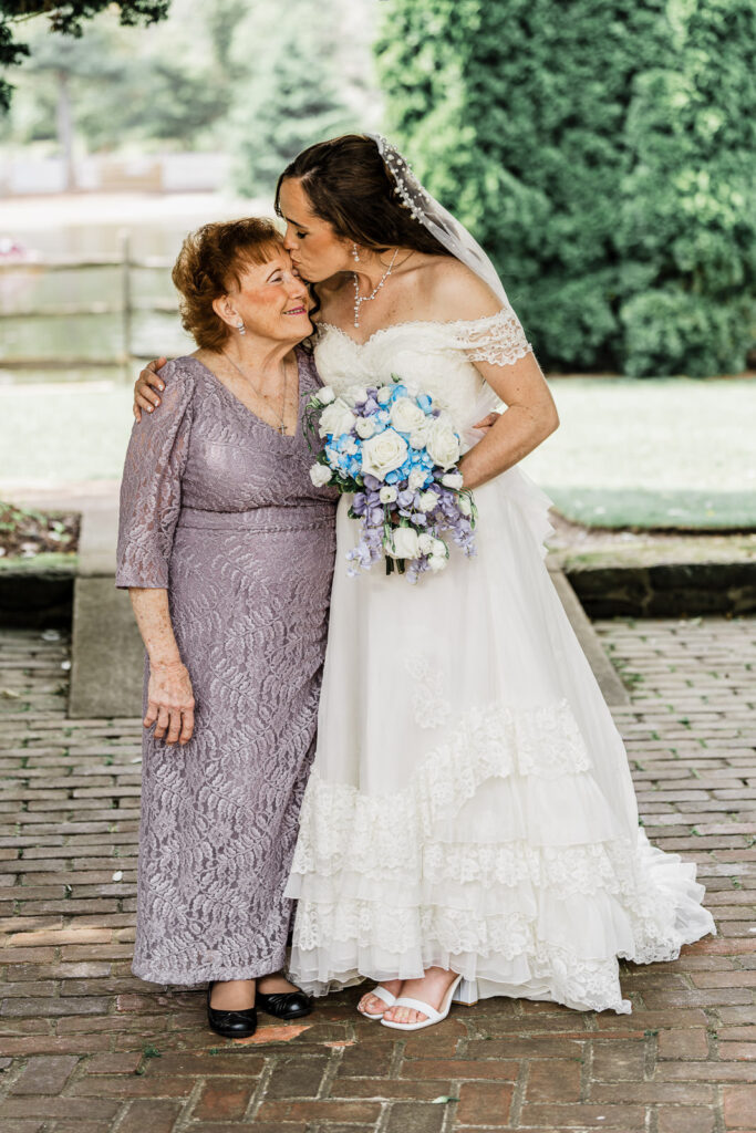 Tender moment of bride kissing mother on forehead in purple lace gown at Smithville Inn wedding in New Jersey by Alex Kaplan Photography