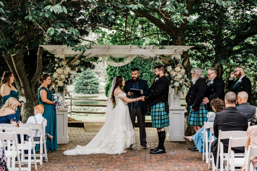 Bride and groom exchanging vows under white pergola with full wedding party at outdoor Smithville Inn ceremony in Absecon New Jersey