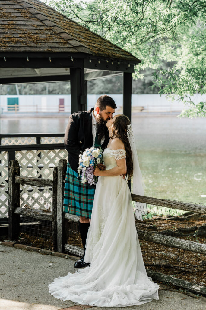 Romantic couple portrait under rustic covered bridge structure near lakeside at Smithville Inn wedding venue in New Jersey