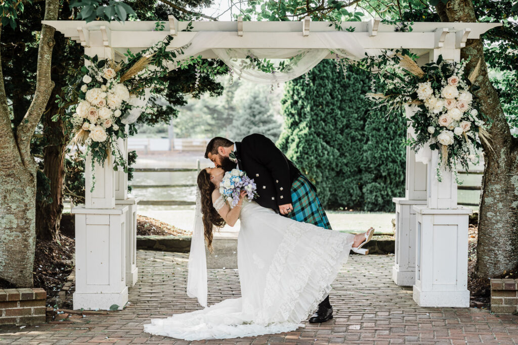Dramatic romantic dip kiss with groom lifting bride under white pergola at Smithville Inn Scottish wedding in New Jersey by Alex Kaplan