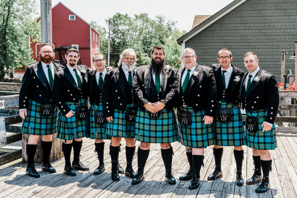 Full Scottish wedding party groomsmen wearing matching tartan kilts and black jackets at Smithville Inn outdoor ceremony location in Absecon NJ