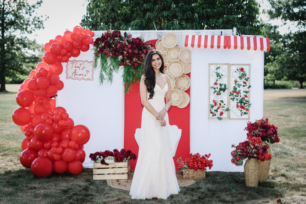 Bride in white gown at Italian-themed engagement party with red balloon arch