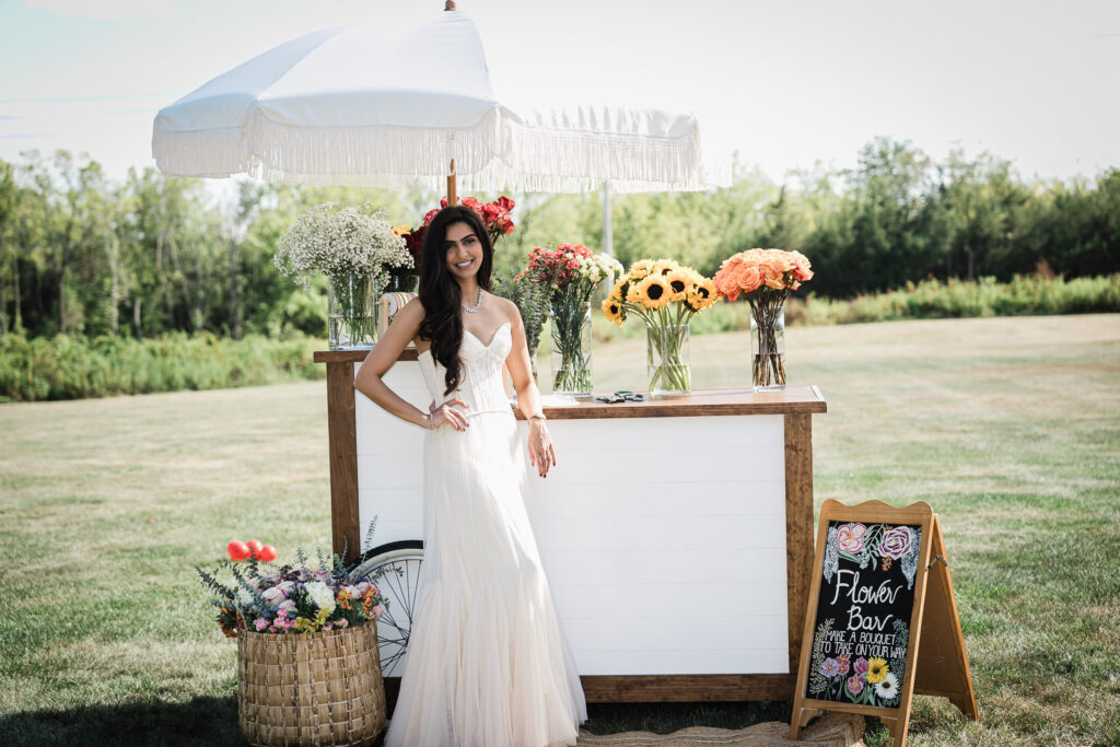Bride at DIY flower bar with umbrella at backyard engagement party