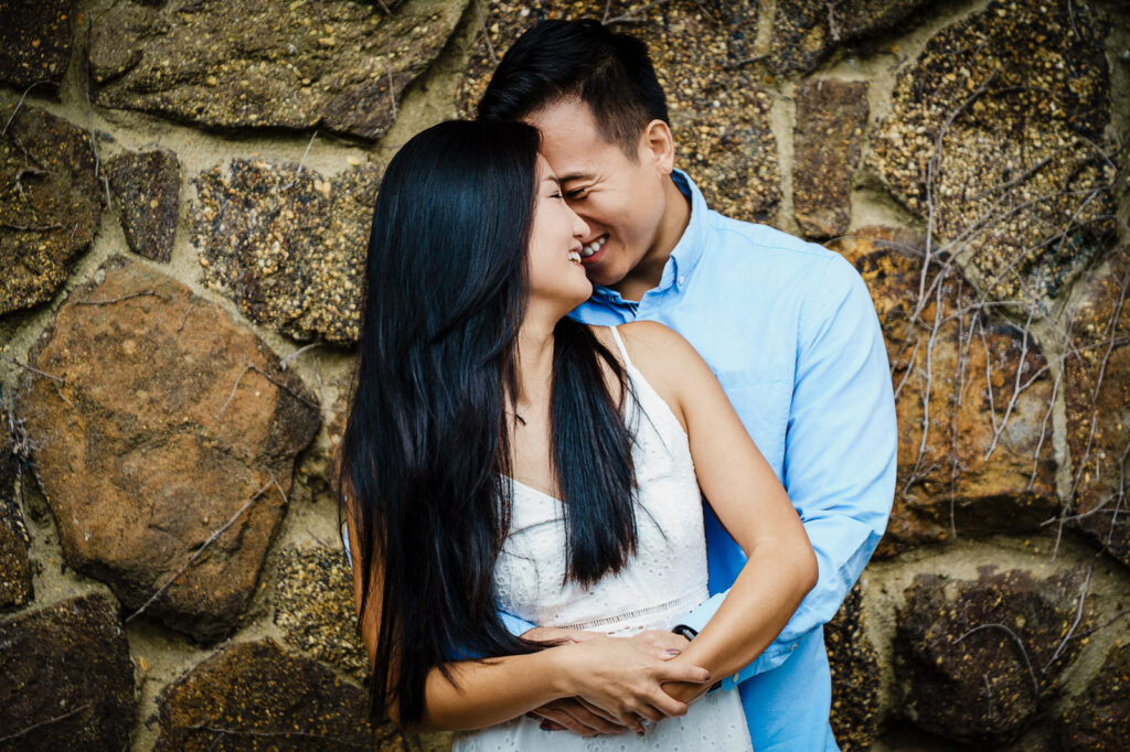 Couple embracing against historic stone wall during Deep Cut Gardens engagement session in Middletown New Jersey