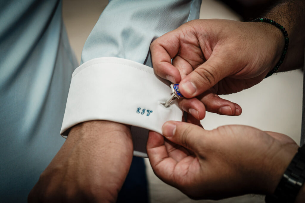 Groom fastening custom RJT monogrammed cufflinks on light blue shirt