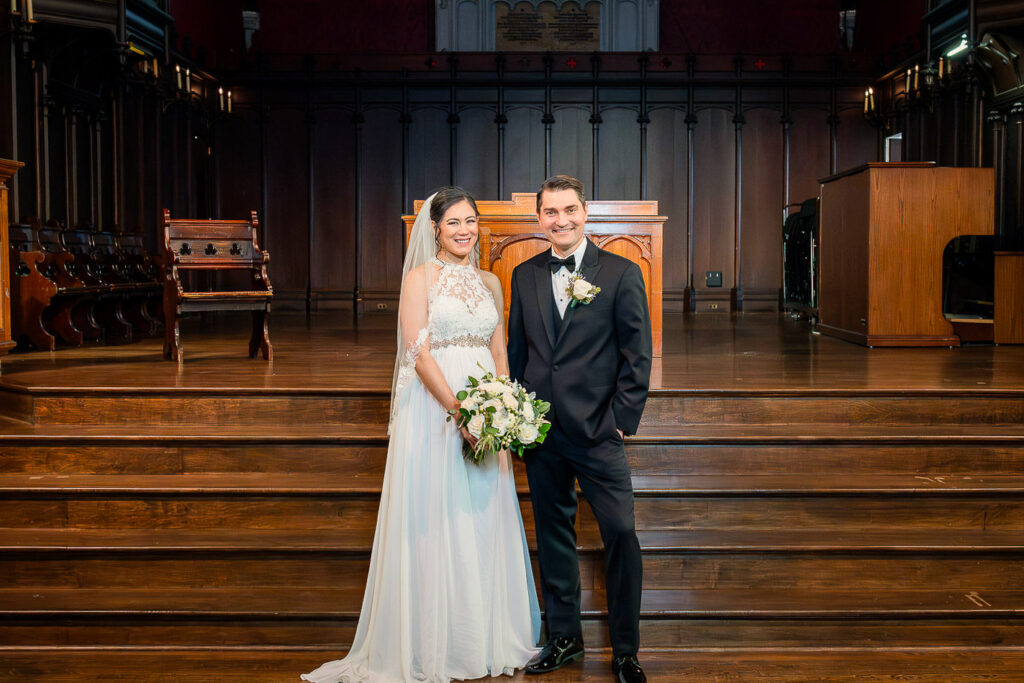 Wedding couple portrait on altar at Kirkpatrick Chapel with ornate wooden architecture and stained glass window by Alex Kaplan Photography New Brunswick