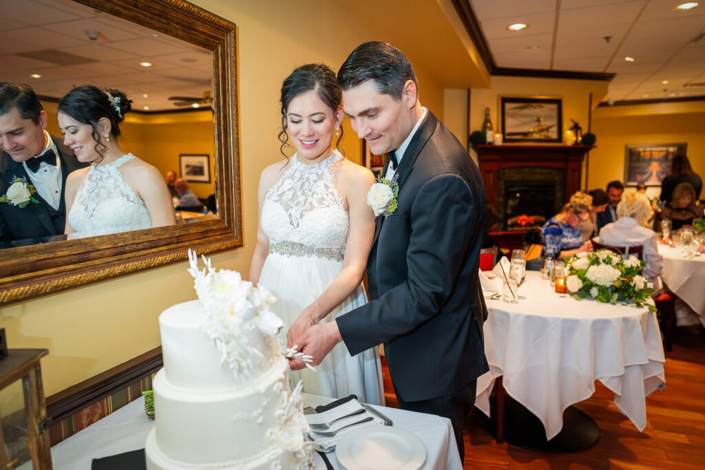 Happy couple cutting three-tier white wedding cake with sugar flowers at Steakhouse 85 reception in New Brunswick, photographed by Alex Kaplan