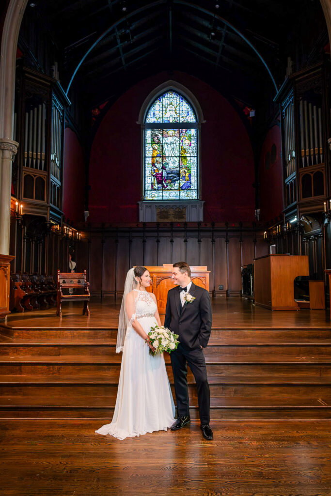 Candid moment of bride and groom sharing a look on Kirkpatrick Chapel altar with colorful stained glass window, Alex Kaplan wedding photographer