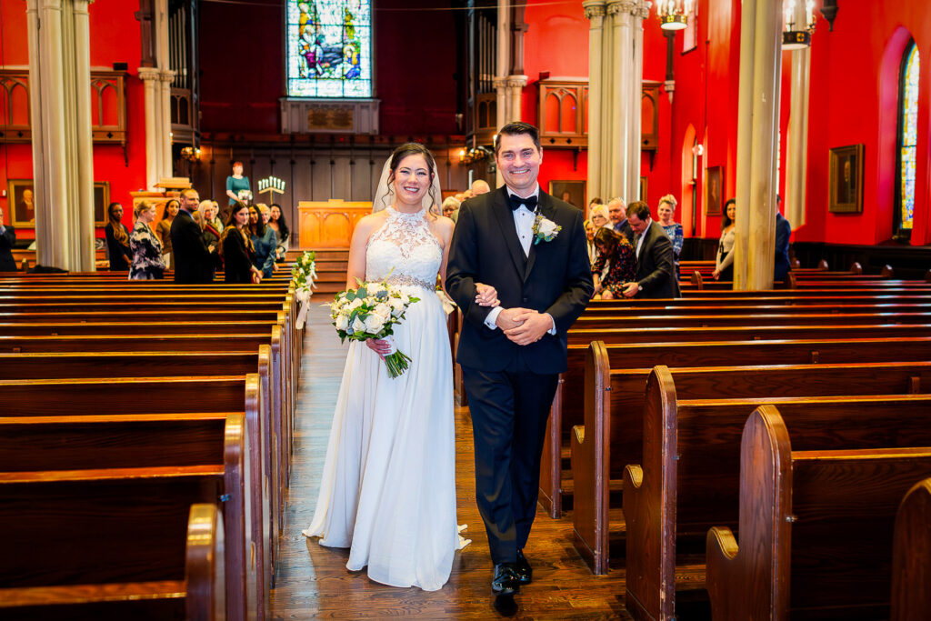 Bride and groom walking down the aisle during recessional at Kirkpatrick Chapel wedding with dramatic red walls and guests celebrating, photographed by Alex Kaplan Photography