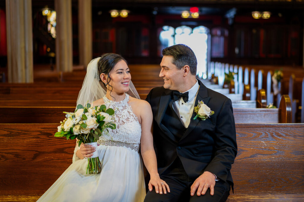 Wedding couple portrait in Kirkpatrick Chapel pews with dramatic red walls and organ pipes, photographed by Alex Kaplan Photography