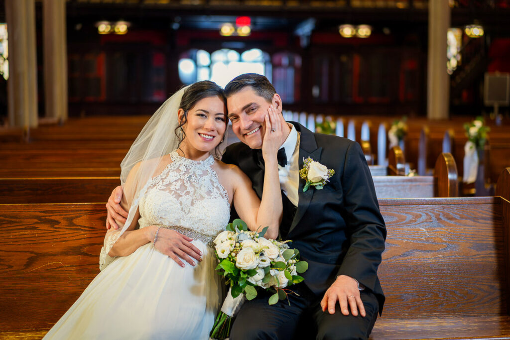 Close-up of bride and groom sharing loving moment in Kirkpatrick Chapel pew with blurred stained glass background, Alex Kaplan photographer