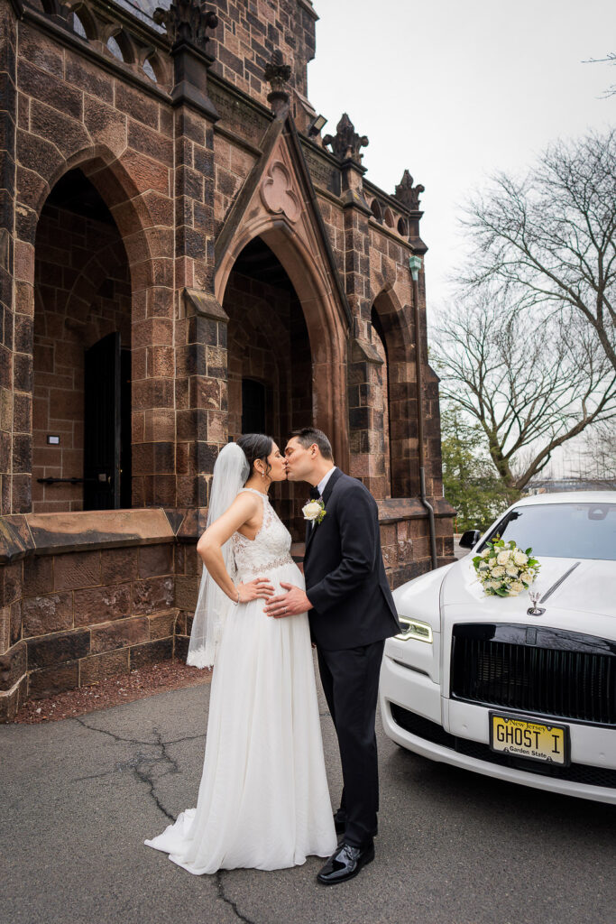 Bride and groom kissing by Rolls Royce Ghost outside Kirkpatrick Chapel with brownstone Gothic arches, Alex Kaplan wedding photographer