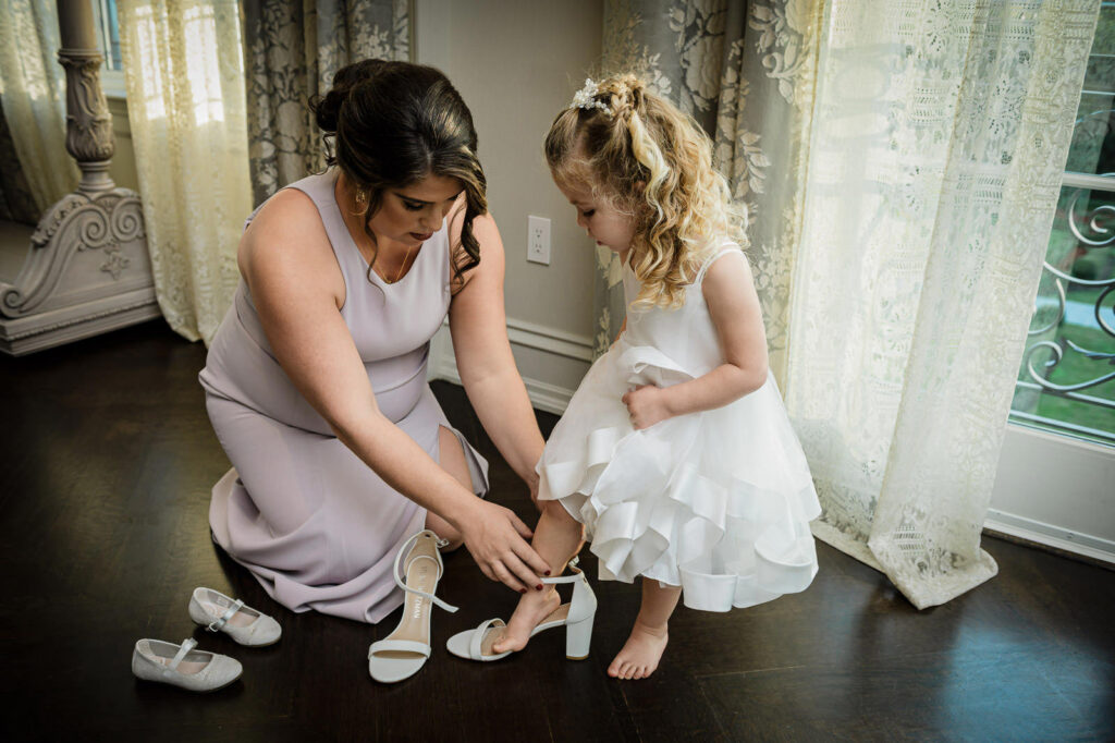 Bridesmaid helping flower girl with shoes at Park Chateau wedding East Brunswick NJ