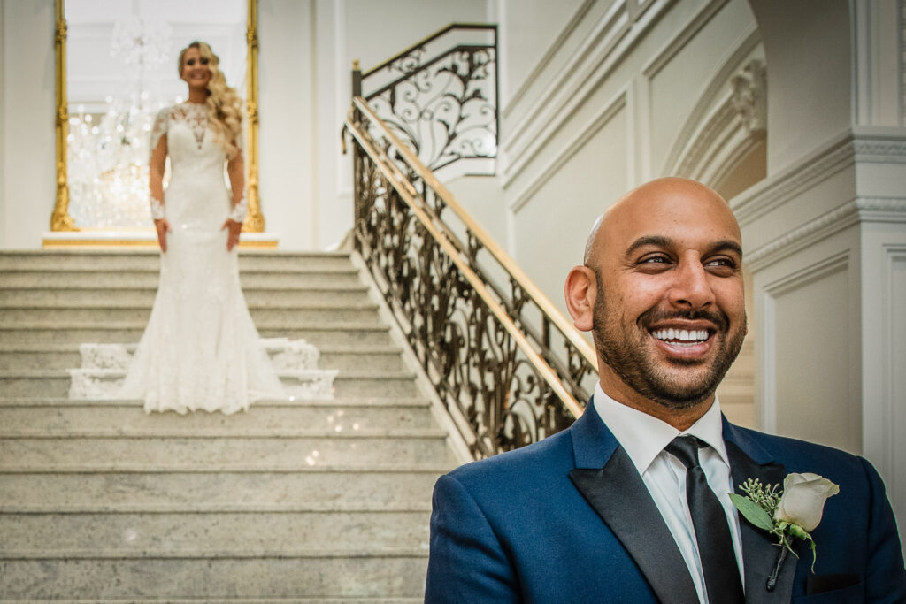 First look moment on grand staircase with ornate iron railings at Rockleigh Country Club