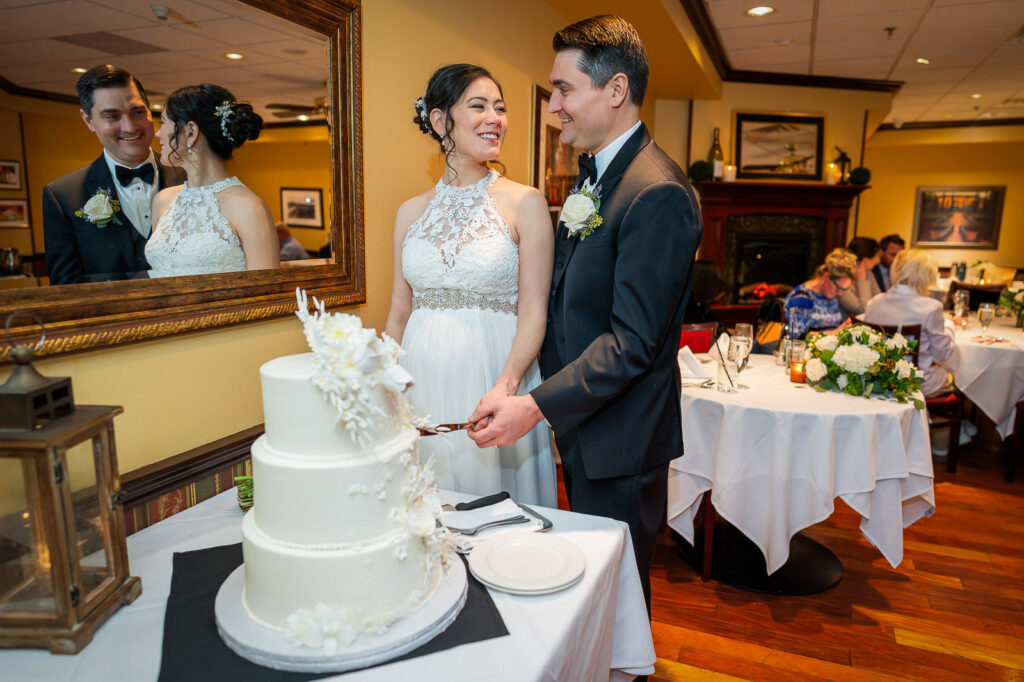 Bride and groom cake cutting moment at Steakhouse 85 reception with elegant white floral wedding cake, New Brunswick wedding by Alex Kaplan Photography