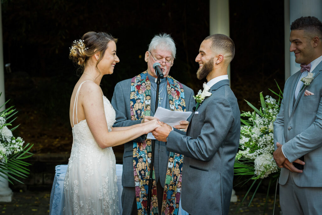 Couple exchanging vows with officiant in distinctive floral vest during outdoor Tides Estate ceremony